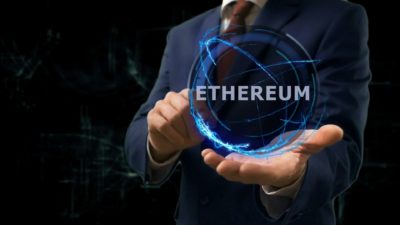 a headless man in a business suit holds out his palm where a graphic image of a sphere appears with the word 'Ethereum' while his other hand points to it amid a dark background.