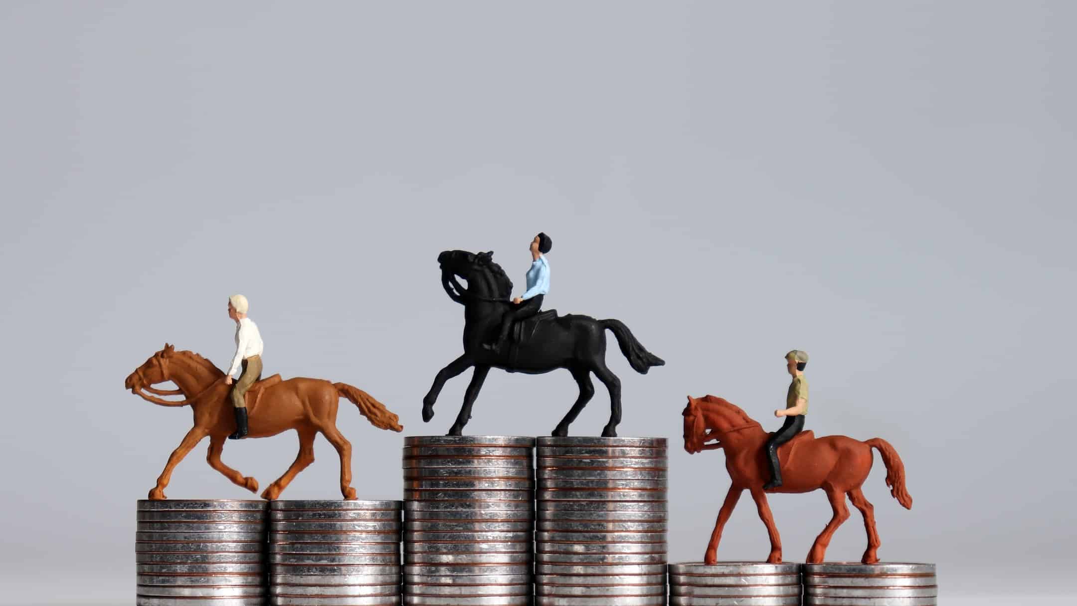image of three small model horses with riders on top of stacks of coins of various heights.