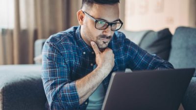 A man holds his hand under his chin as he concentrates on his laptop screen and reads about the ANZ share price