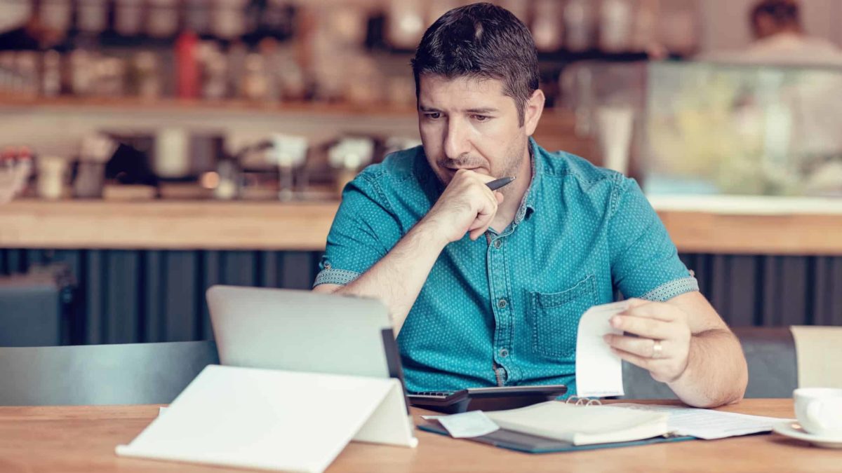 Man ponders a receipt as he looks at his laptop.