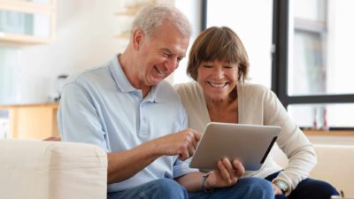 A happy couple looking at an iPad feeling great as they watch the Challenger share price rise