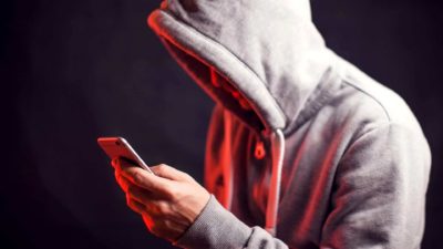 An online scammer looking shady as he operates his mobile phone