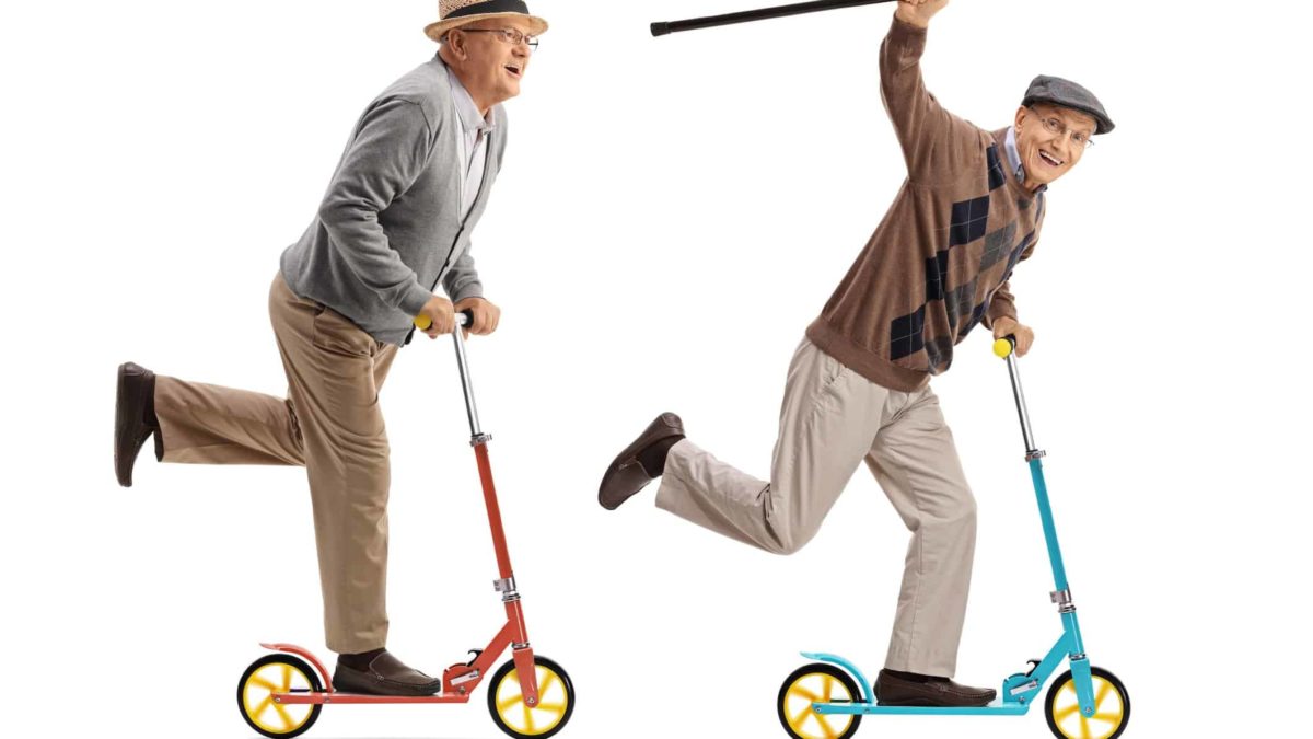 two elderly men smile as the ride past on two wheel scooters with the leader holding his walking stick in the air and smiling broadly for the camera.