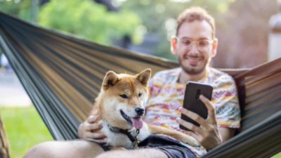 Man on his phone with a shiba inu beside him.