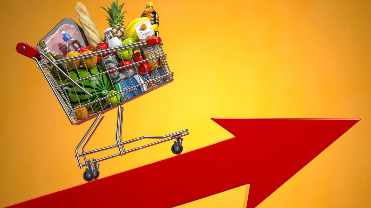 Supermarket trolley with groceries on top of a red pointing arrow.