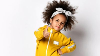 A happy girl in a yellow playsuit with a zip gives the thumbs up