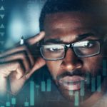 A man is deep in thought while looking at a graph and rising and falling percentages.