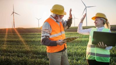 2 workers standing in front of a wind farm giving a high five.