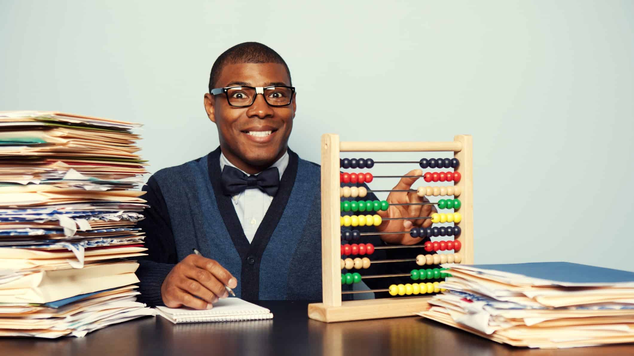 An accountant gleefully makes corrections and calculations on his abacus with a pile of papers next to him.