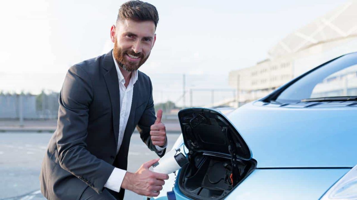 A man wearing a suit and holding an EV charger gives the thumbs up.