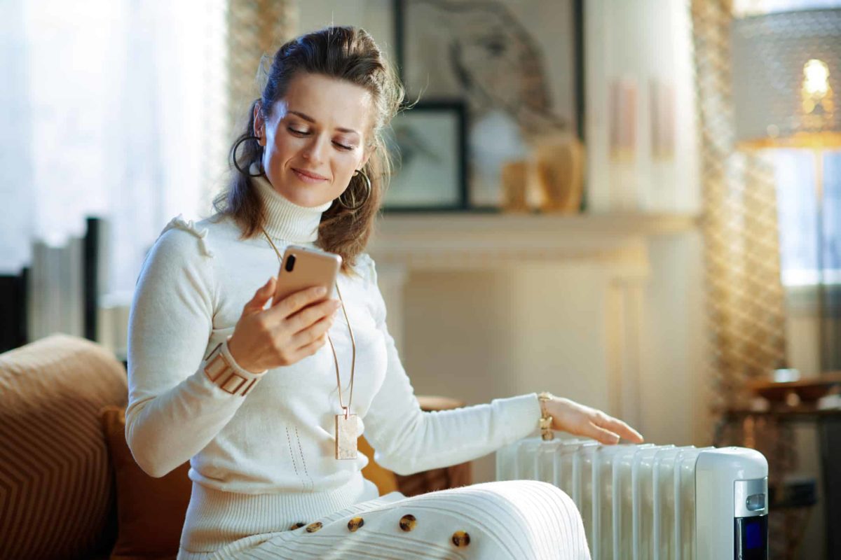 a woman wearing fashionable clothes and jewellery checks her phone with a satisfied smile on her face in a luxurous home setting.