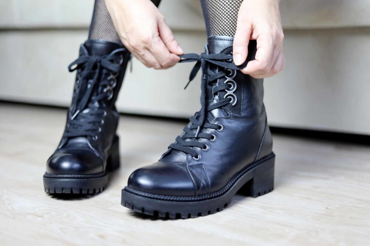 a woman ties up the shoelaces on a fashionable pair of boots that are chunky and shiny.