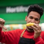 A supermarket employee holds an upside down banana in front of his mouth and his thumbs down as if showing his disapproval of something.