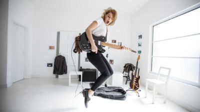 A woman leaps in the air as she shreds on her electric guitar.