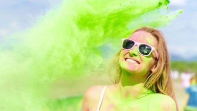 A woman has a big smile on her face as she gets green paint powder tipped all over her.