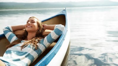A woman lies back and relaxes in her boat with a big smile on her face as it floats on the rising tide.