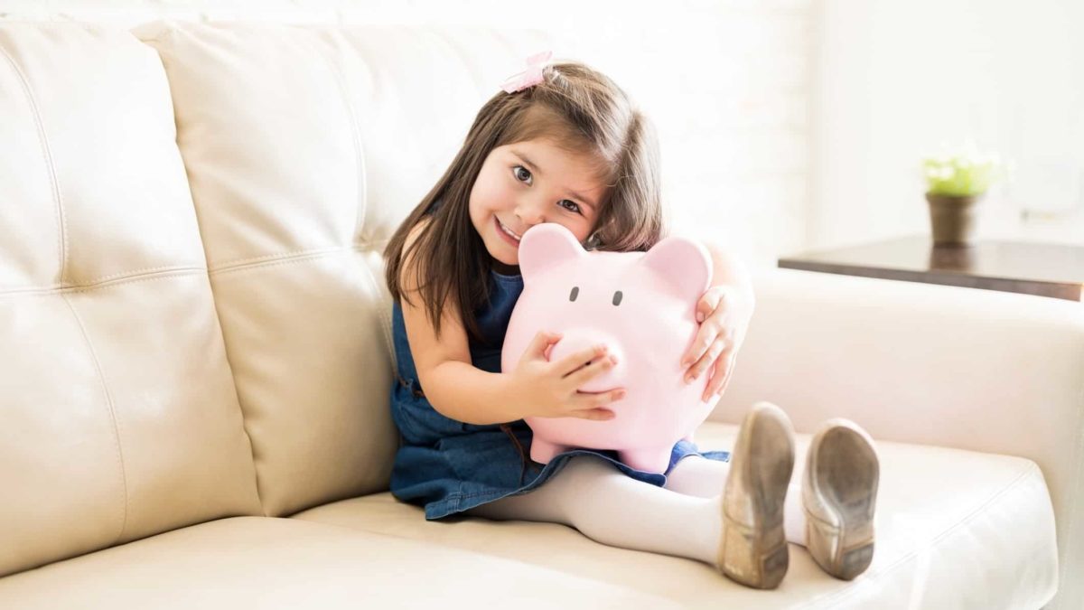 A little girl holds on to her piggy bank, giving it a really big hug.