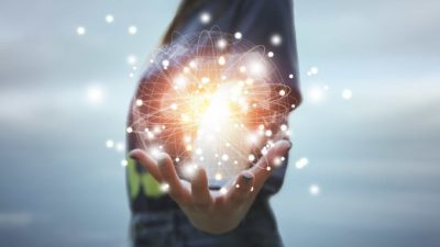 A woman holds a glowing, sparking, technological representation of a planet in her hand.