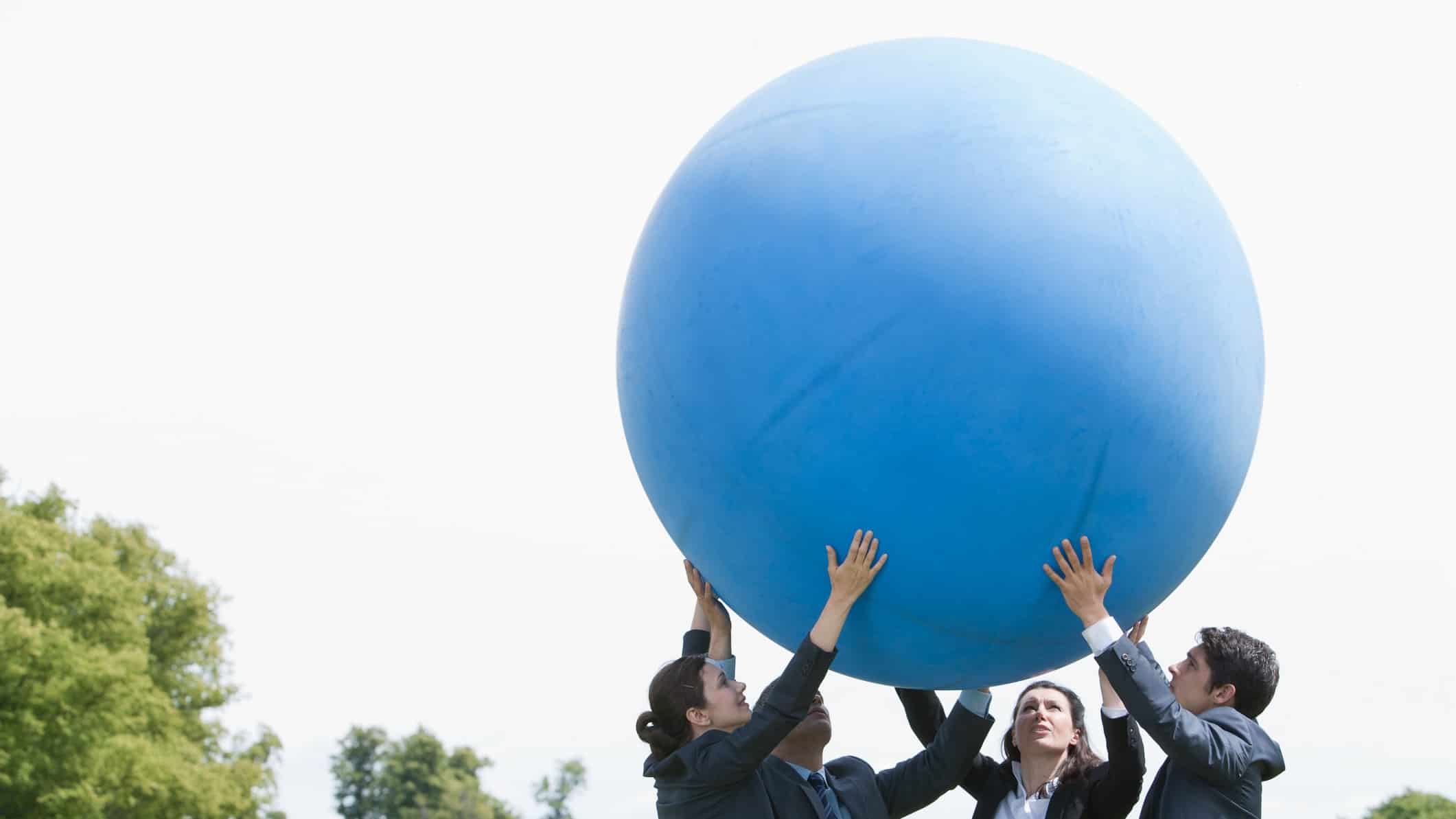 A team lifts a giant inflated ball high into the air, succeeding despite rising inflation.
