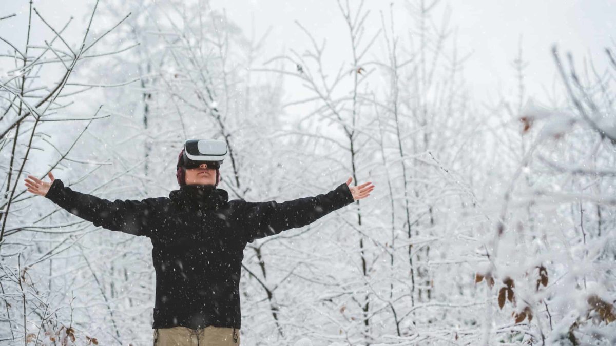A person stands still with a virtual reality technology headset on and arms outstretched, surrounded by frozen ice and snow.