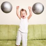 A little boy holds up a barbell with big silver weights at each end.