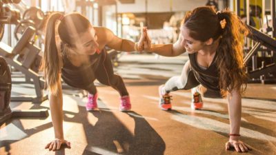 Two girls high five mid-plank, supporting each other at the gym.
