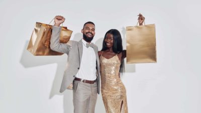 A couple hold up two gold shopping bags.