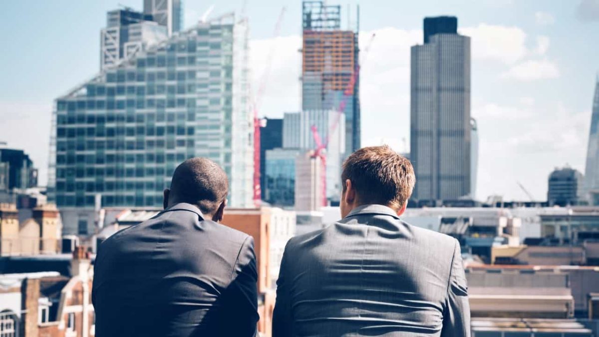 Two businessmen look out at the city from the top of a tall building.