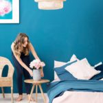 A woman sets flowers on a side table in a beautifully furnished bedroom.