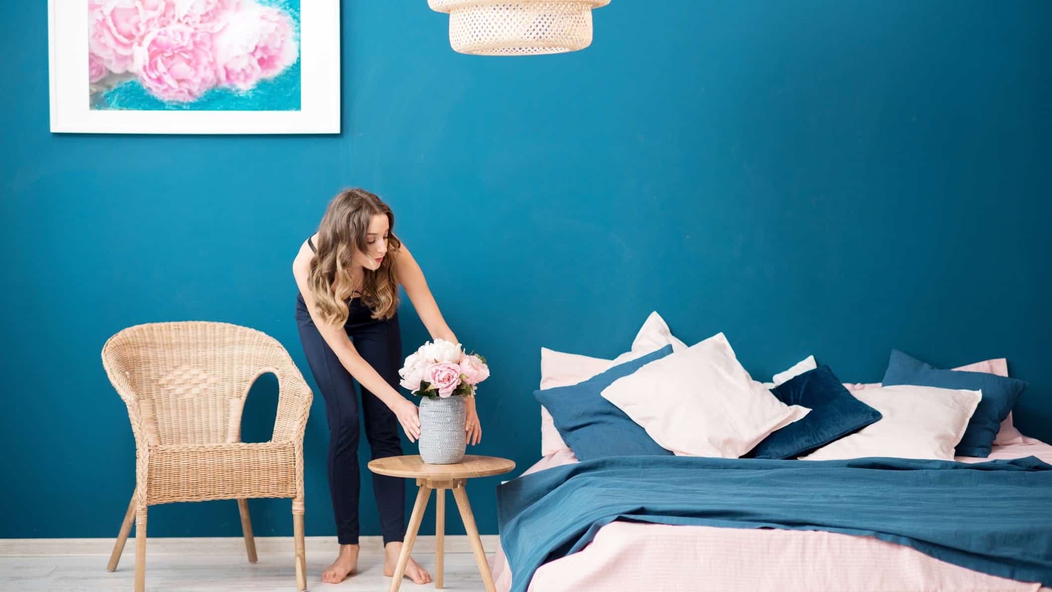A woman sets flowers on a side table in a beautifully furnished bedroom.