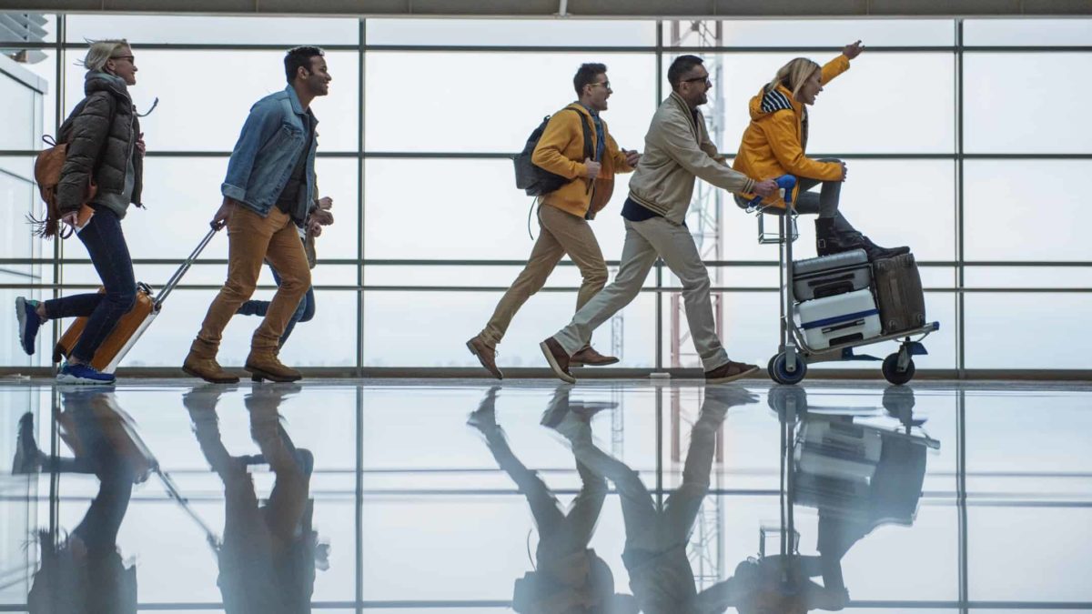 a group of people walk rapidly in a line with airport trolleys and carting baggage as they appear to excitedly set off at the airport on a trip.