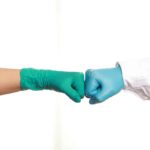 Two people wearing gloves giving each other a fist bump.
