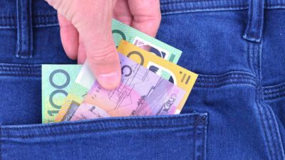 Close-up photo of a back jean pocket with Australian dollar bills in it and a hand reaching in to collect the notes