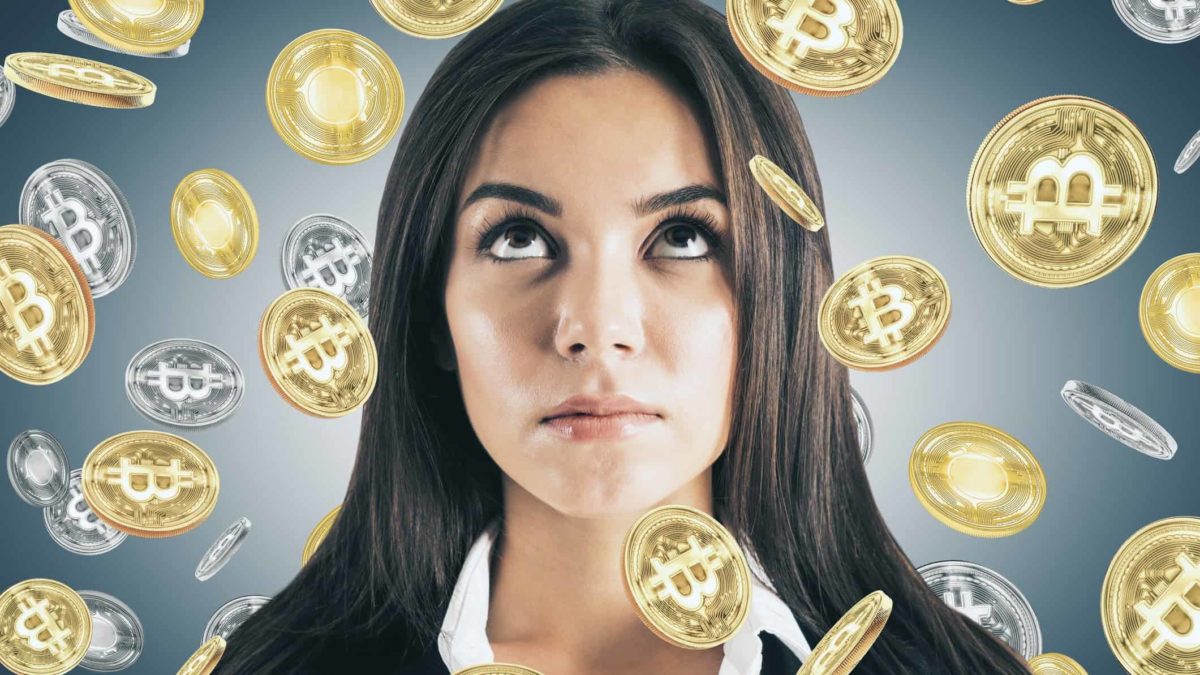 a close up of a woman's face looks skywards as she is showered in a sea of graphic symbols of gold and silver coins bearing the bitcoin logo.