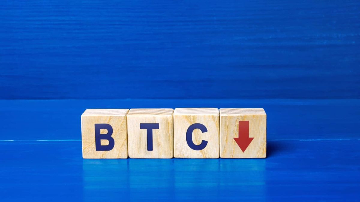BTC spelt out on wooden blocks with a red sign going down.