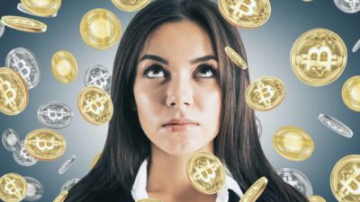 a close up of a woman's face looks skywards as she is showered in a sea of graphic symbols of gold and silver coins bearing the bitcoin logo.