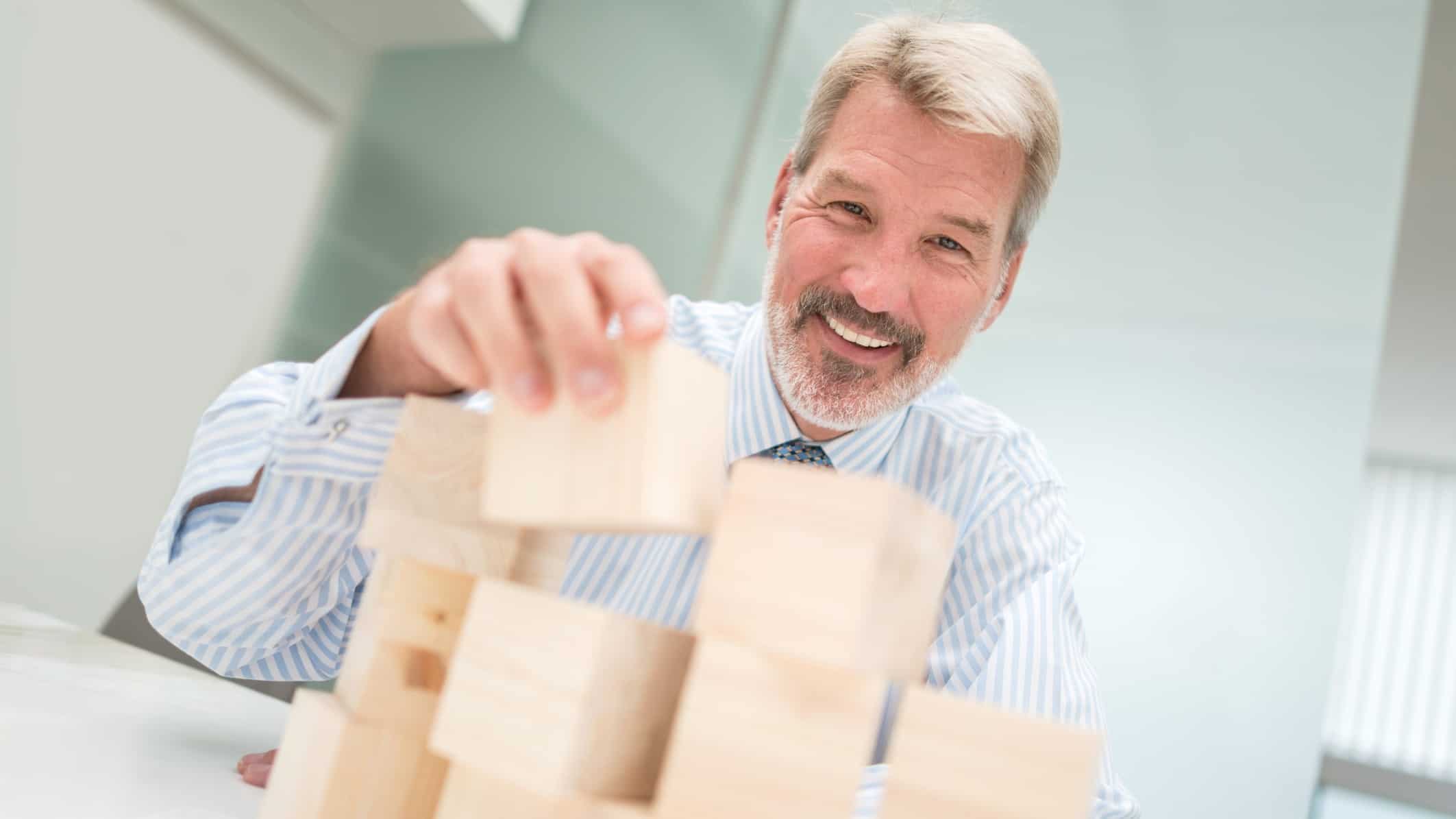 A businessman stacks building blocks while smiling about the anticipated 7% dividend yield that CSR is expected to pay based on its current share price