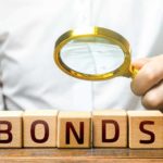 A magnifying glass on wooden blocks spelling out bonds.