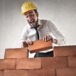 A man lays a brick on a wall he is building with a look of joy on his face.