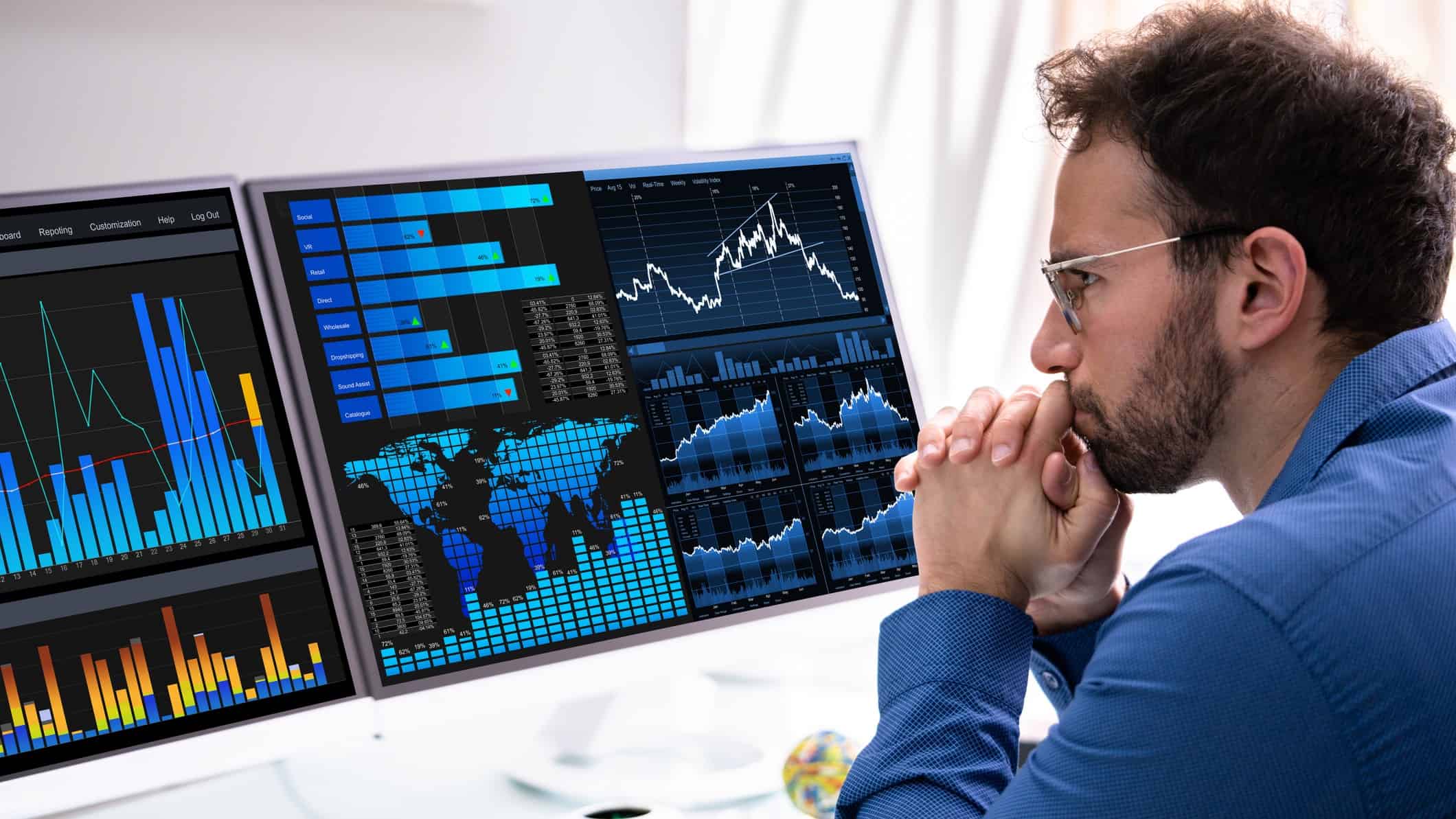 An analyst wearing a dark blue shirt and glasses sits at his computer with his chin resting on his hands as he looks at the CBA share price movement today