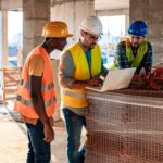Three builders analyse their blueprints on site.