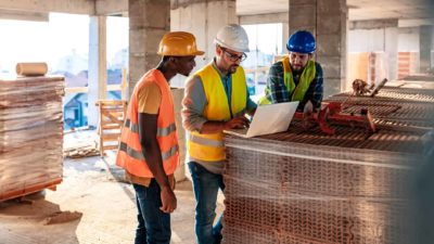 Three builders analyse their blueprints on site representing the growth in the Johns Lyng share price