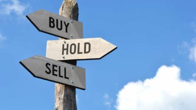 Buy, hold and sell ratings written on signs on a wooden pole.