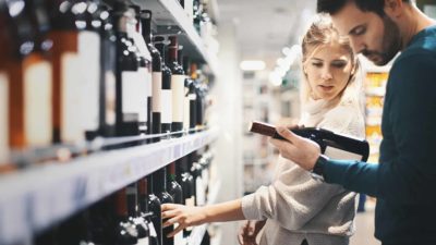 Couple look at a bottle of wine while trying to decide what to buy.