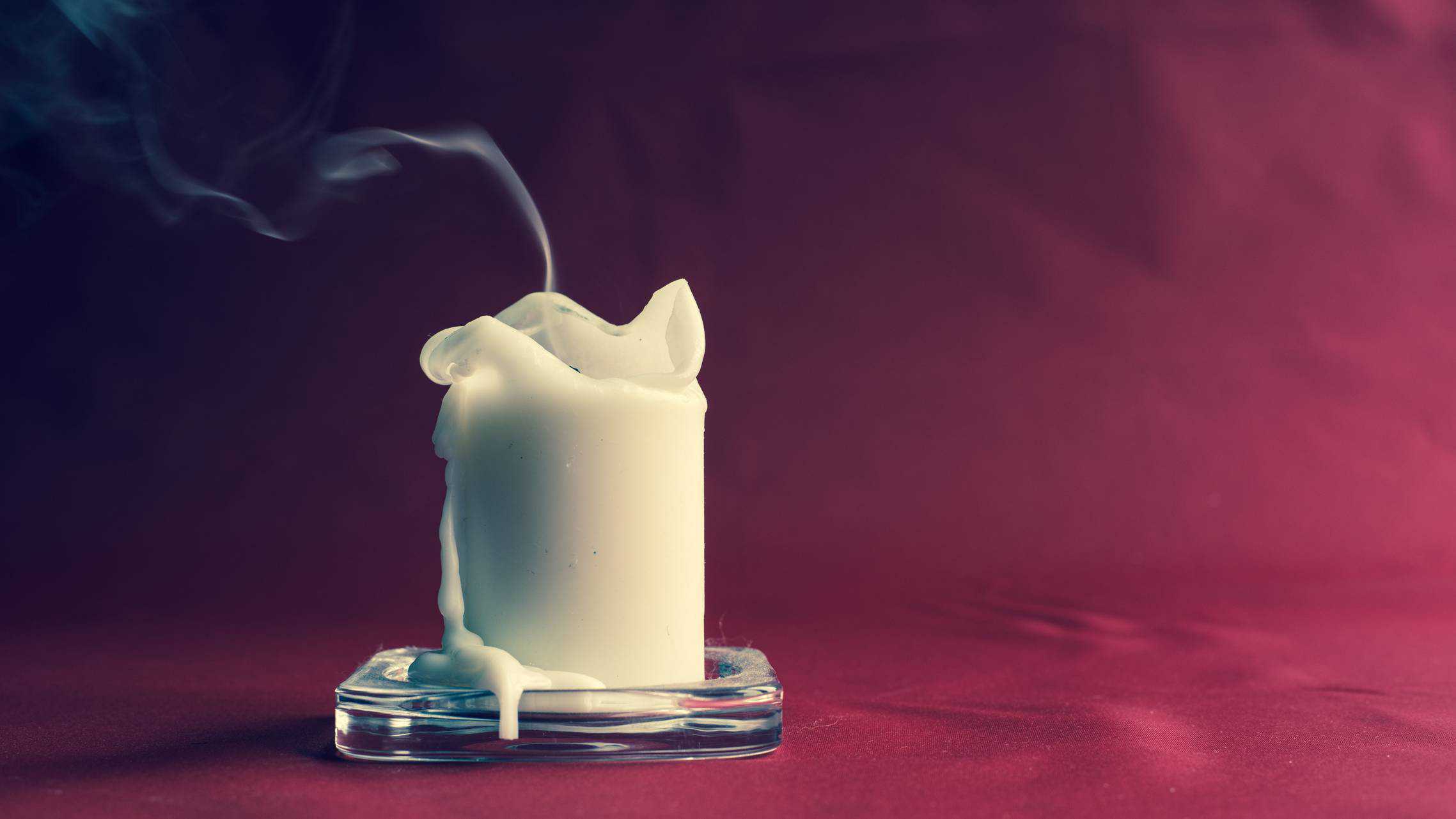 A smouldering white candle with a burgundy background indicating the falling Dusk share price today