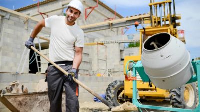 A smiling tradie shovels cement into a mixer on a building site