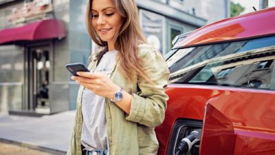 Happy woman on her phone while her electric vehicle charges.