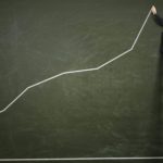 Man on a ladder drawing an increasing line on a chalk board symbolising a rising share price.