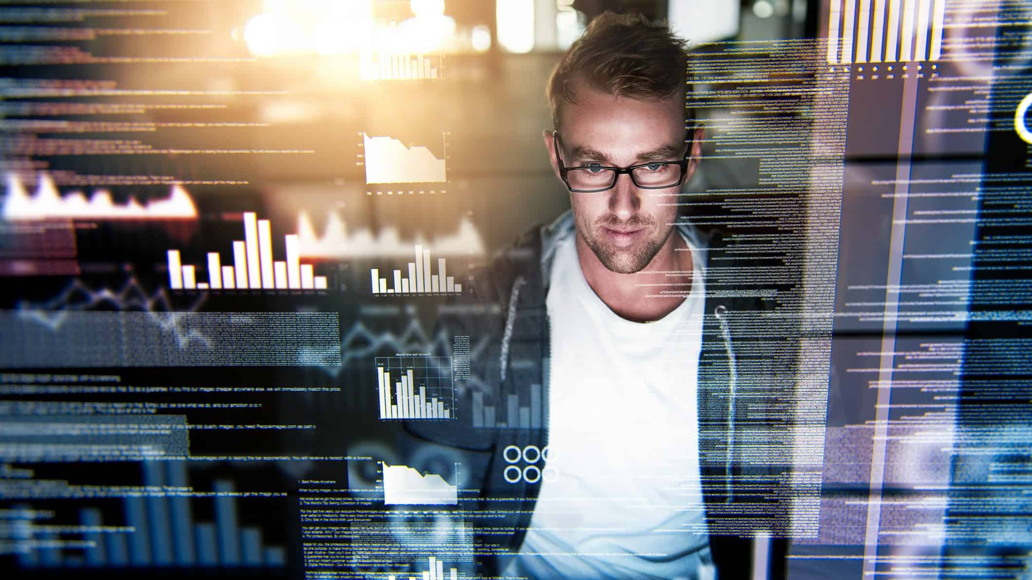 a man sits in casual clothes in front of a computer amid graphic images of data superimposed on the image, as though he is engaged in IT or hacking activities.