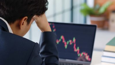 Disappointed man with his head on his hand looking at a falling share price his a laptop.